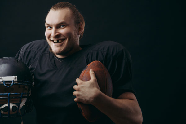 Football player smiling while holding a football and wearing a helmet, representing the risks of avulsions during contact sports.